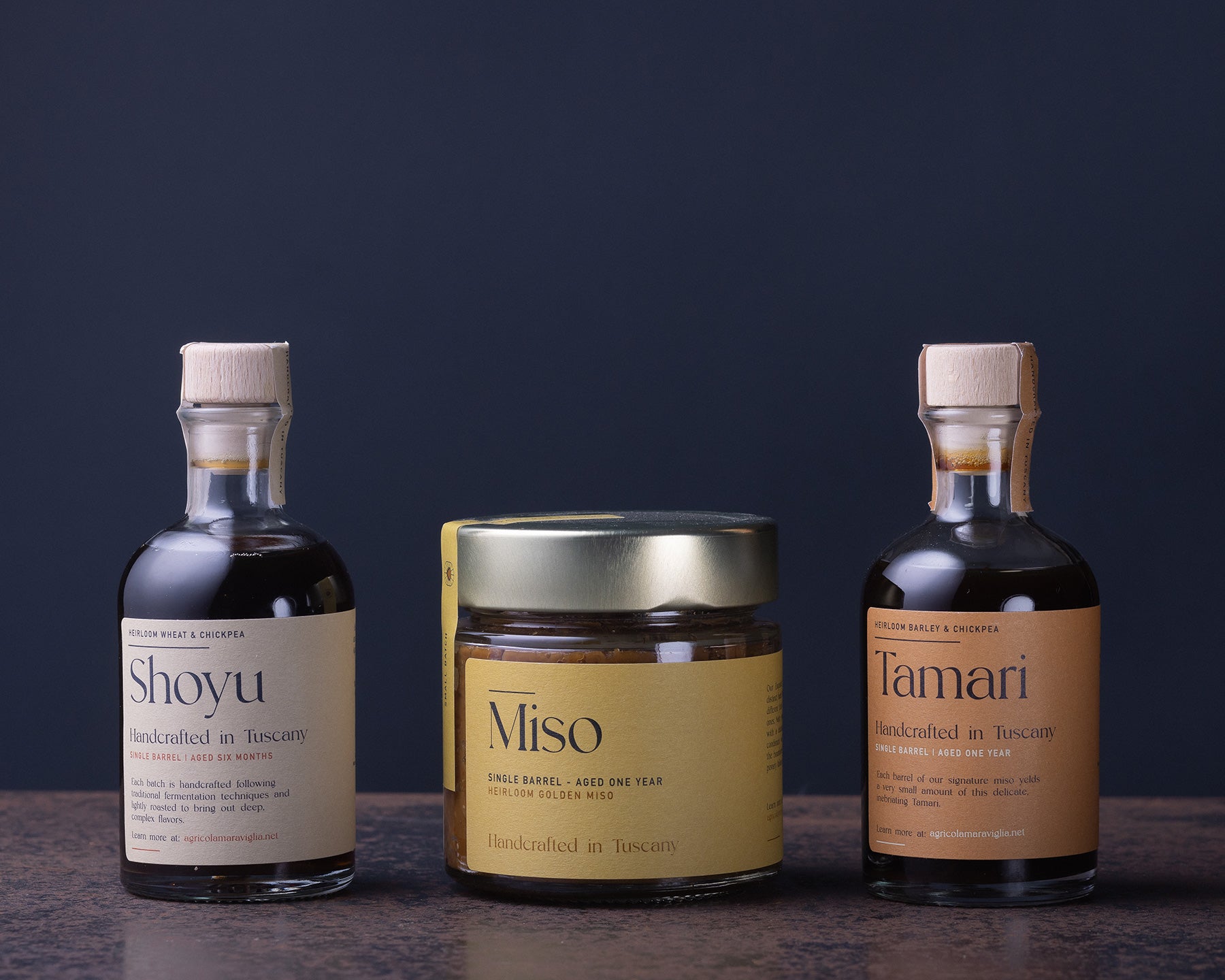 Three bottles and a jar Tuscan Shoyu, Miso, and Tamari from Agricola Maraviglia on a dark background